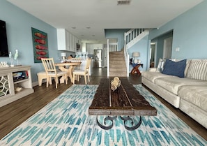 A living room with a wooden coffee table, a sofa, a dining area with chairs, and a staircase leading to another level.
