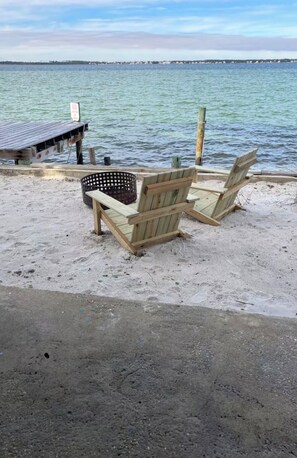 Eine Holzsteganlage mit einem 'Nichtschwimmen'-Schild, zwei Adirondack-Stühlen und einem sandigen Strandabschnitt.