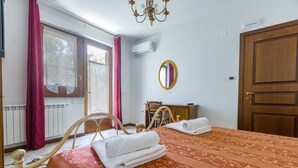 A hotel room with a bed, a wooden chair, a table, a mirror, and a door. - Room 'Ghiro' with Mountain View, Wi-Fi and Air Conditioning (Sant'Angelo di Brolo)