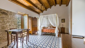 A room with a bed, a table, chairs, a chandelier, and a stone wall. - 'Arcaloro Resort Infinito' Room with Mountain View and Hot Tub (Sant'Angelo di Brolo)
