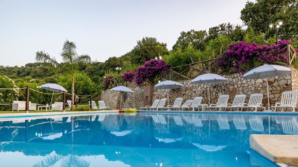 A swimming pool with lounge chairs and umbrellas, surrounded by stone walls and purple flowers. - 'Arcaloro Resort Infinito' Room with Mountain View and Hot Tub (Sant'Angelo di Brolo)