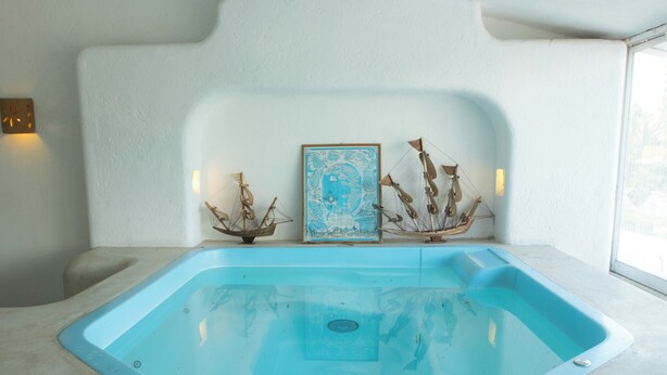 Un bain à remous rectangulaire, avec un intérieur bleu clair, deux sculptures en forme de navire et une carte encadrée accrochée au mur derrière.