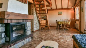 Un interior rústico con chimenea, escalera de madera, comedor y una cama.