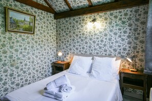Een net opgemaakt bed met witte lakens, twee bedlampjes en een lijst met een afbeelding aan de muur.