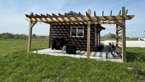 Eine Holzhütte mit einer Pergola, einem Grill und einem Tisch mit Stühlen vor der Tür.