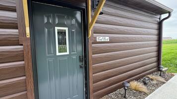 A wooden exterior with a dark grey door, a nameplate reading "Teal Nest," and a small garden area with mulch and plants.
