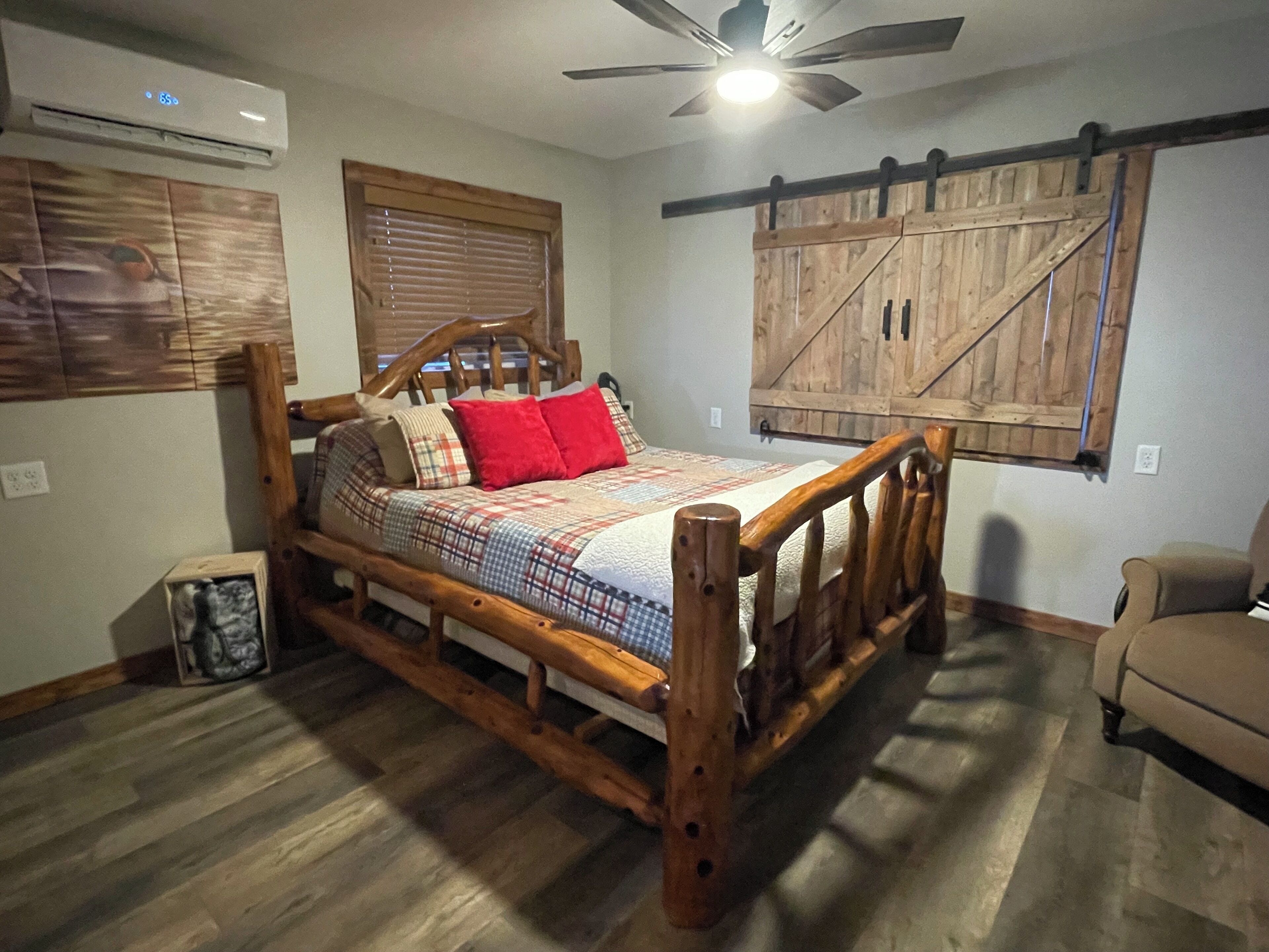 Una camera da letto con un letto con struttura in legno, una ventola a soffitto, un mobile a parete in stile granaio e un piccolo settimino in legno.