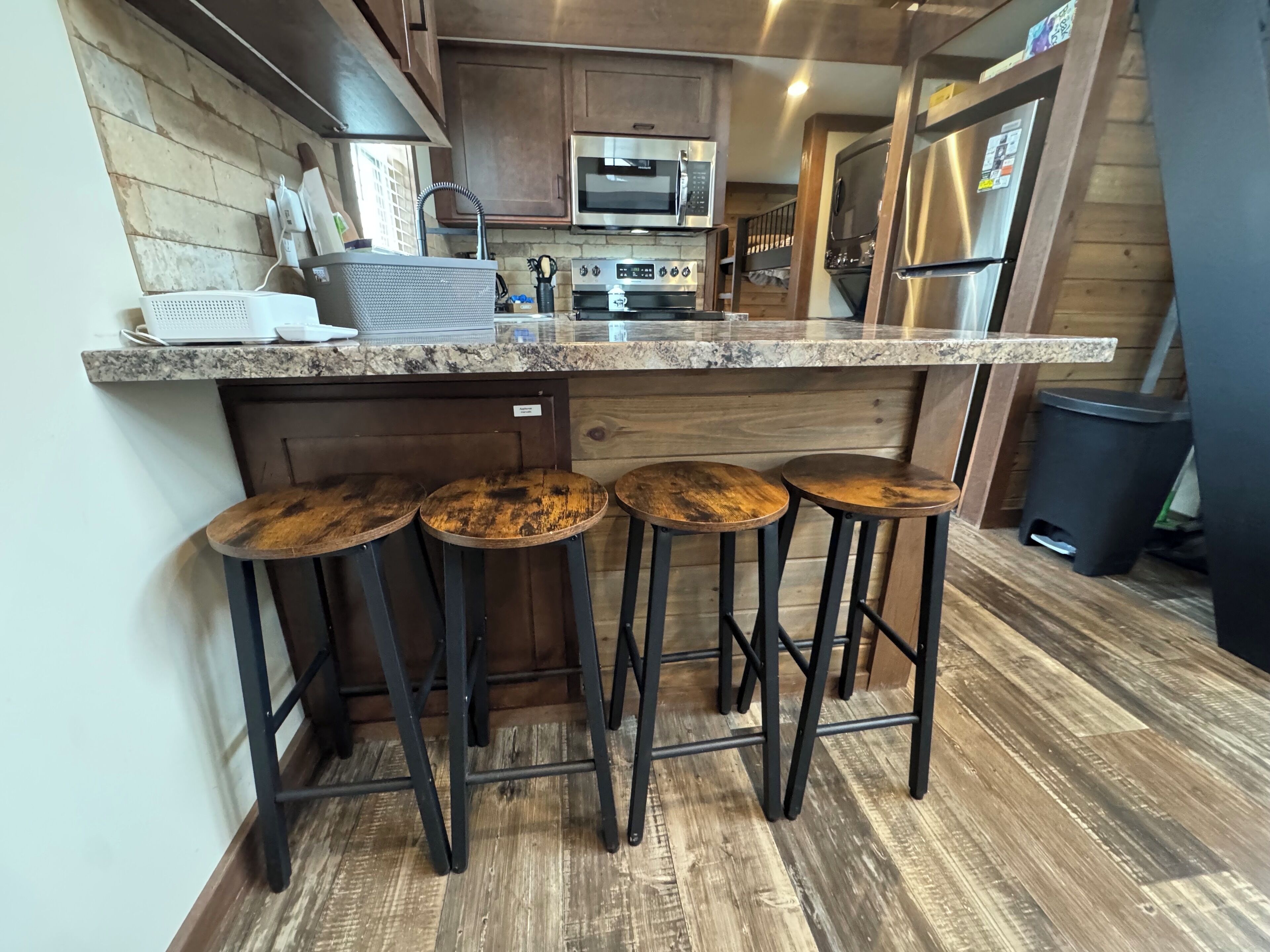 Una cocina con encimera de granito, electrodomésticos de acero inoxidable y taburetes de madera.