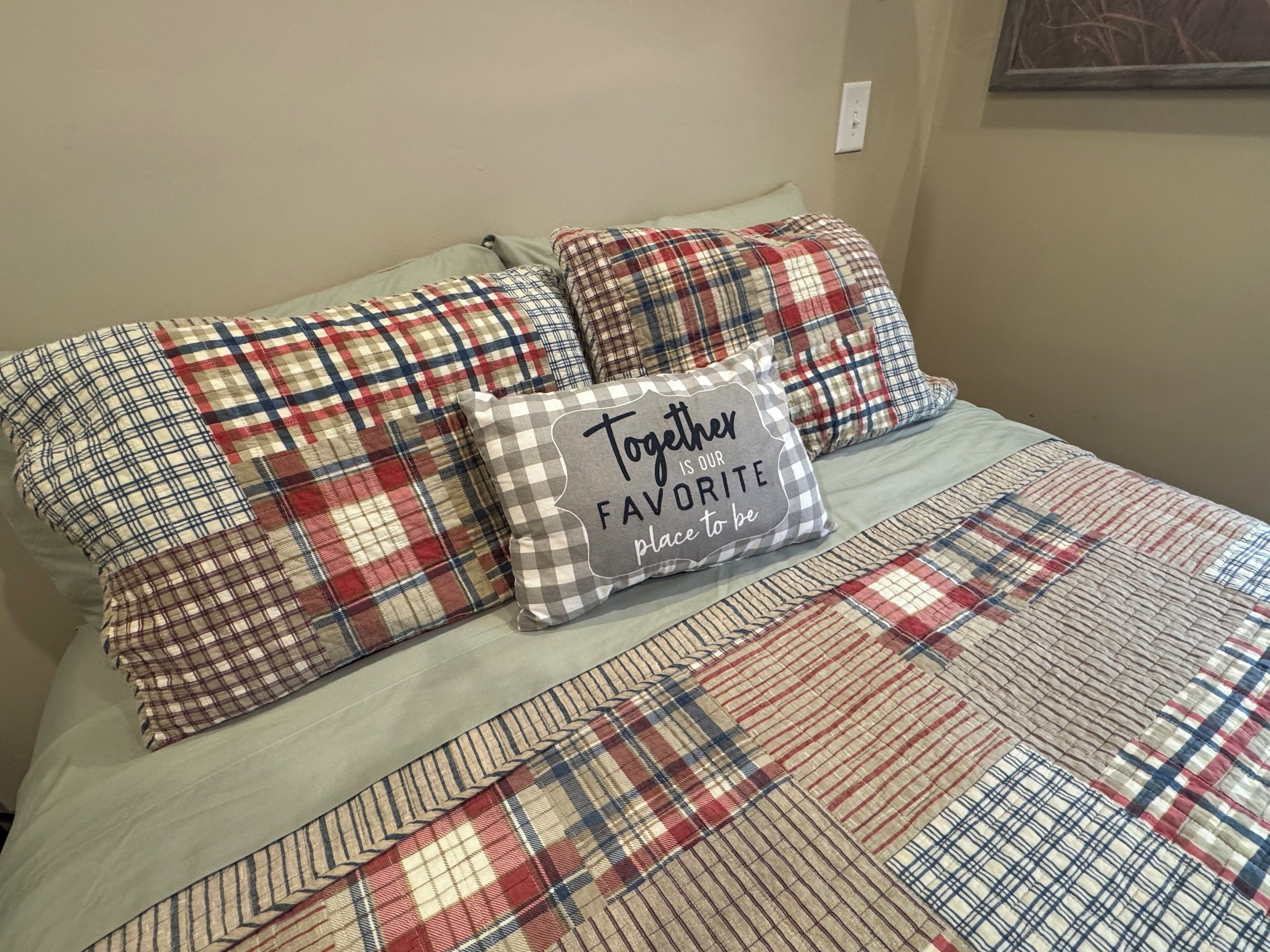 A bed with plaid bedding and a pillow with the text "Together is our favorite place to be."