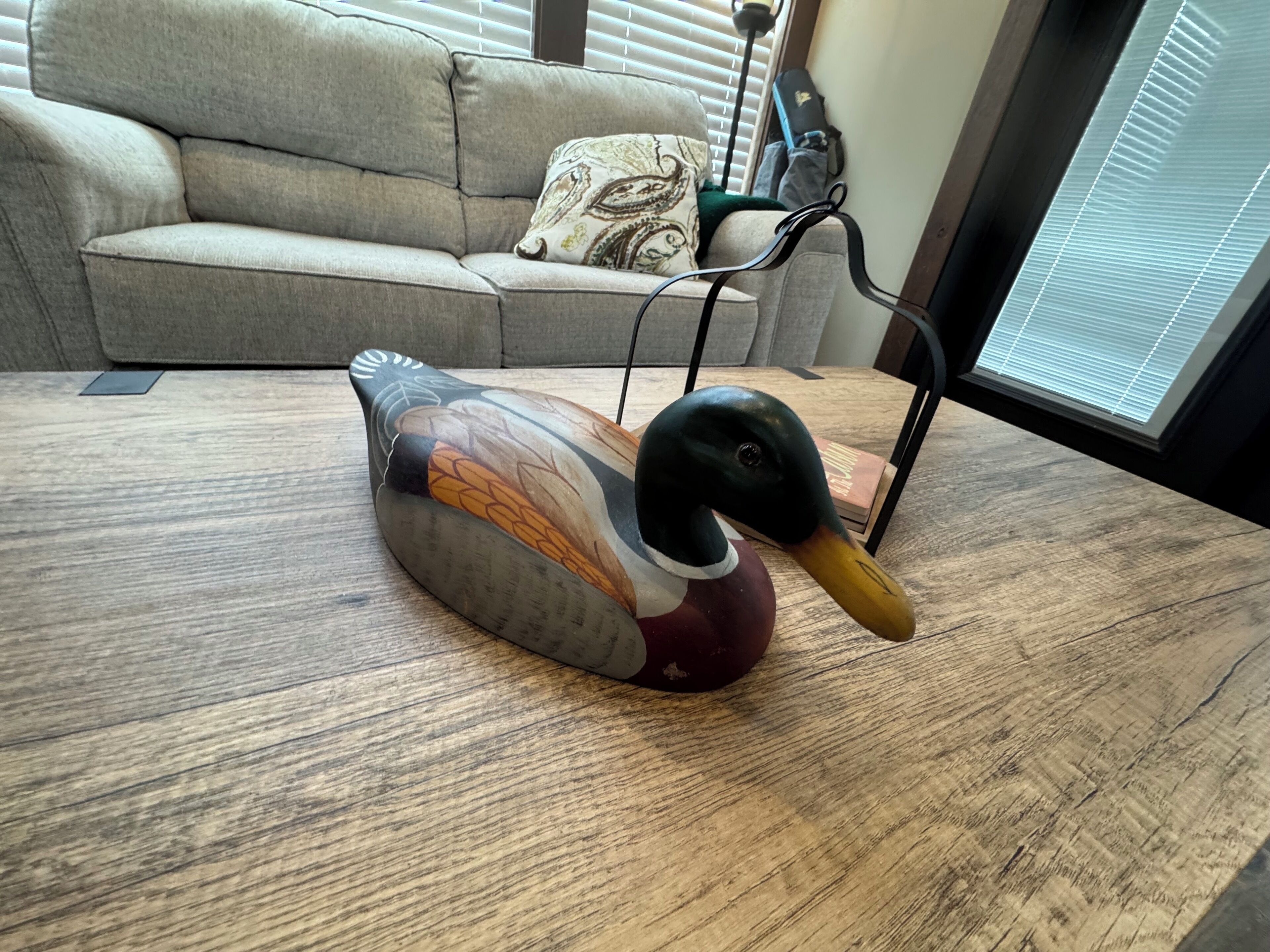 Eine schwanenartige Figur auf einem Holztisch in einem Raum mit einer Couch und Jalousien.