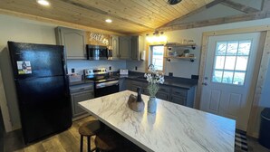 Una cocina con isla de mármol, techo de madera y un cartel que dice 'Gather' sobre el microondas.