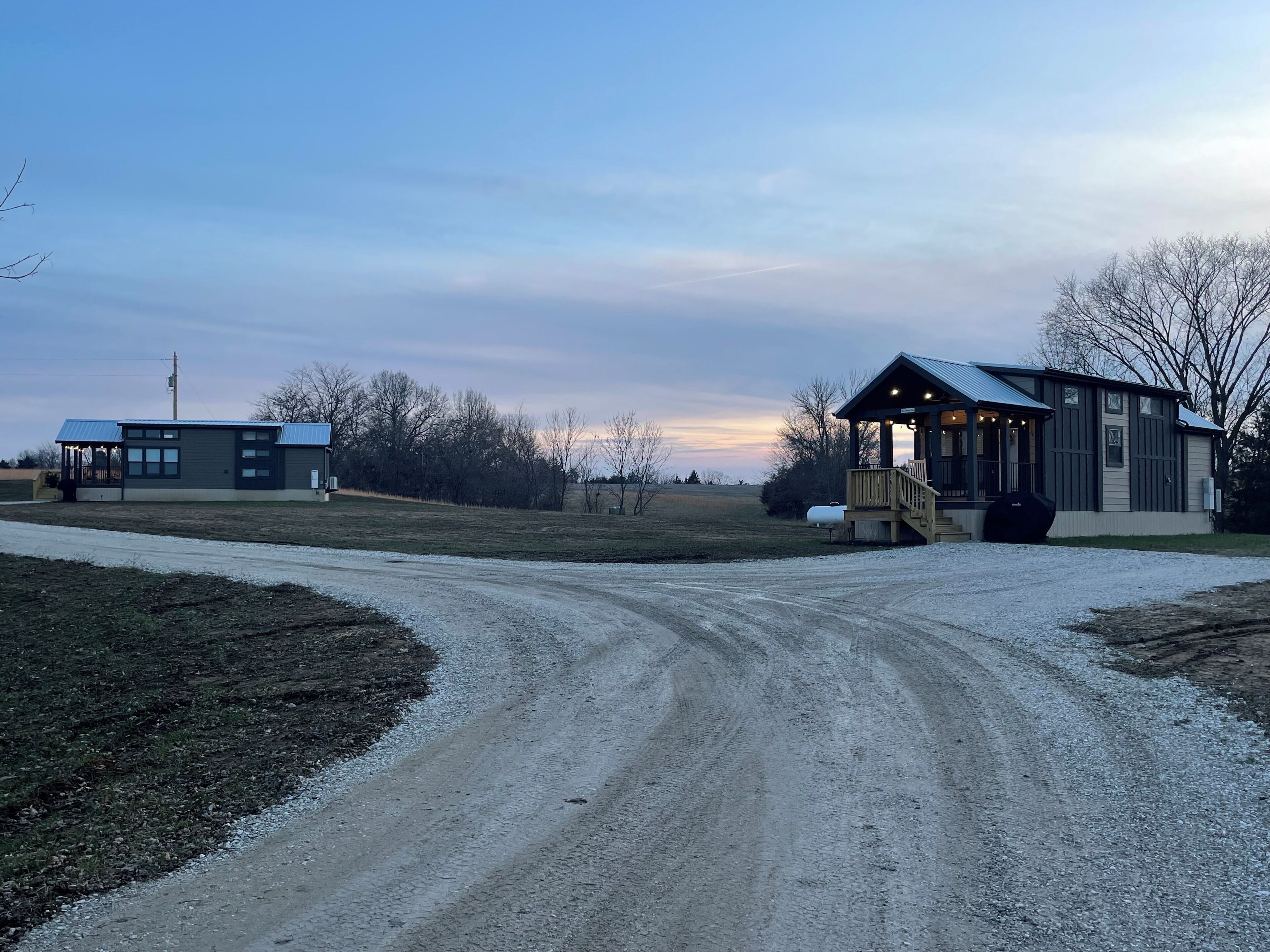 A gravel road leading to a building with a porch and a covered area.