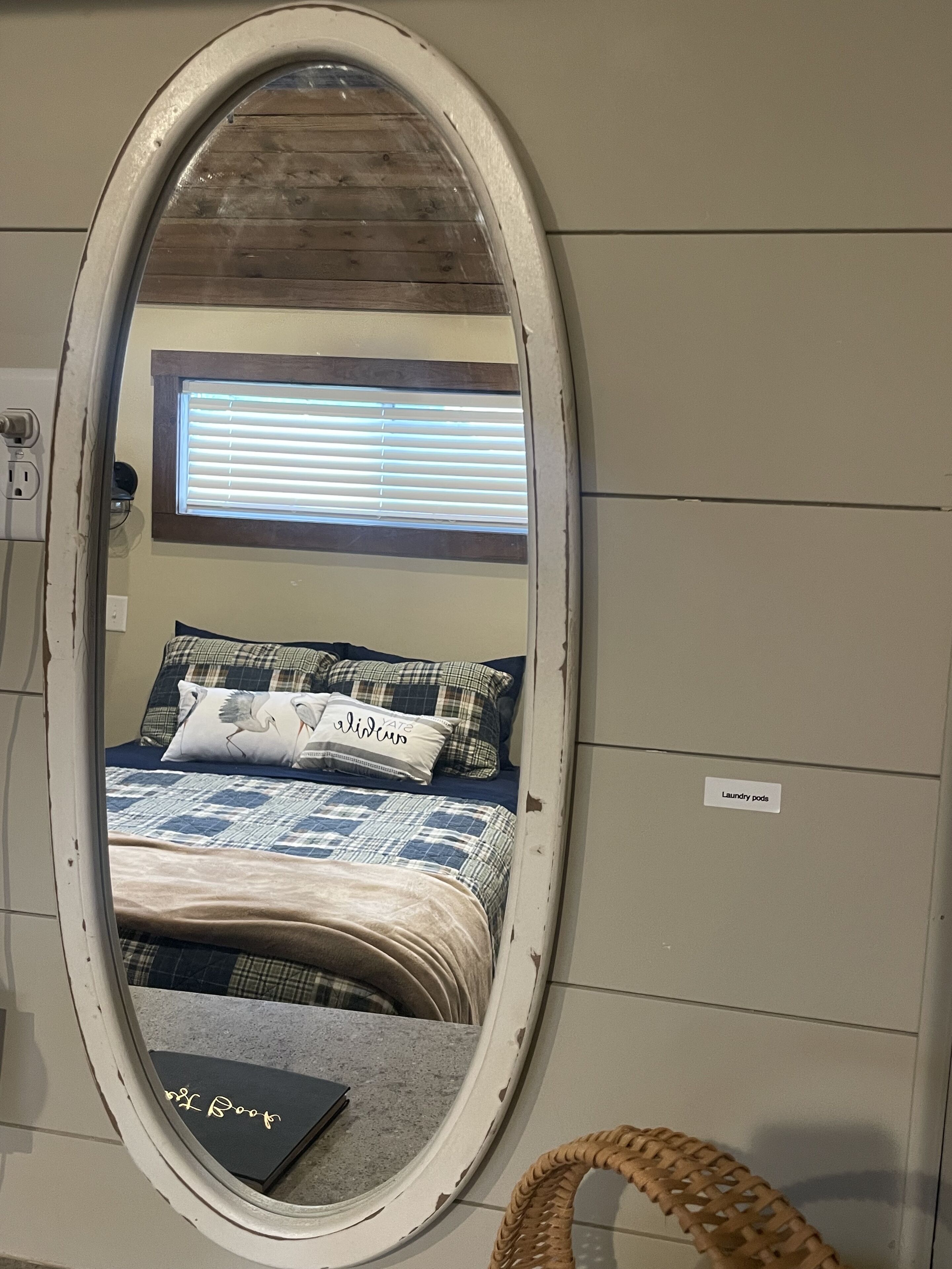 Ein Schlafzimmer mit Bett, Spiegel, Fenster mit Jalousien, Nachttisch mit Buch und einer Beschriftung an der Wand.