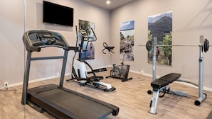 Une salle de sport équipée d’un tapis de course, d’un vélo elliptique, d’un vélo d’appartement et d’un banc de musculation.