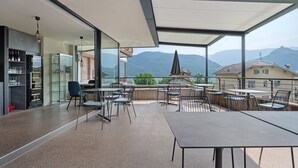 A modern outdoor dining area with tables and chairs, a bar with shelves, and a view of mountains. - Room 'Weinbergblick' with Mountain View, Shared Pool and Wi-Fi (Caldaro)