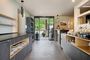 Een moderne keuken met uitzicht op de omgeving, met een aanrecht, borden, een koffiehoek en een schuifdeur naar een terras.