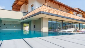 A modern building with a swimming pool, glass walls, and a wooden deck. - Room 'Seaberhof 6' with Lake View, Shared Pool and Wi-Fi (Caldaro)