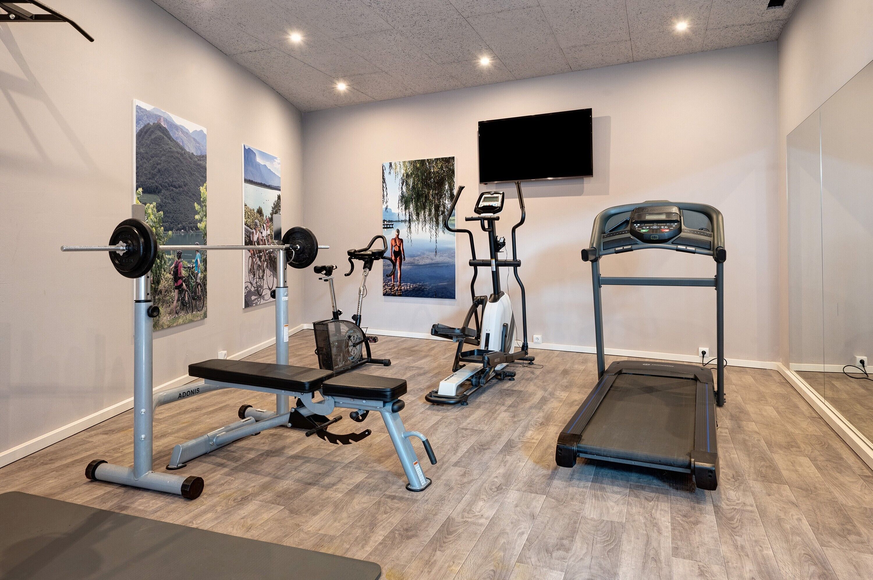 Een sportschool met een loopband, elliptische trainer en een gewichtbank.