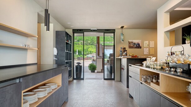 A modern kitchen with a view to the outdoors, featuring a counter with plates, a coffee station, and a sliding door leading to a patio. - Room 'Seaberhof 6' with Lake View, Shared Pool and Wi-Fi (Caldaro)