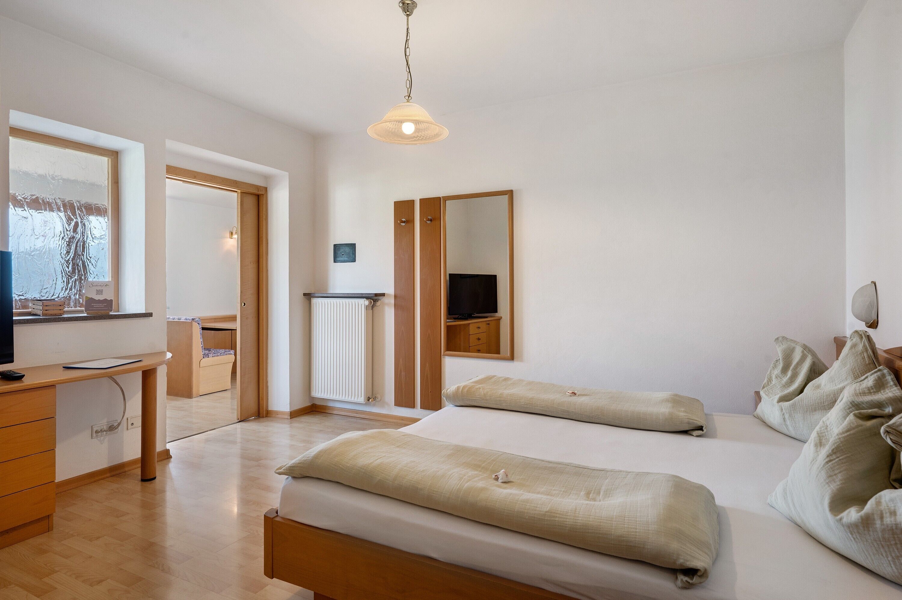 A bedroom with a bed, bedside tables, a desk, a mirror, and a television.