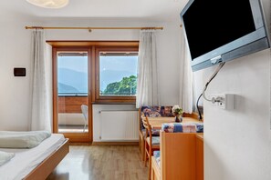 A room with a bed, a dining table with chairs, a television, and a view of mountains through a window.