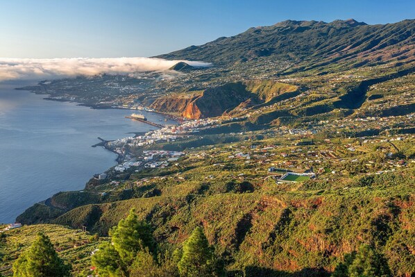 Un pueblo costero con montañas al fondo, un puerto y una mezcla de edificios residenciales y comerciales.