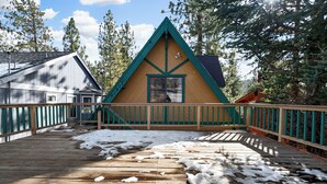A wooden cabin with a triangular roof, surrounded by a wooden deck and snow. - Little Bear Lodge (Big Bear Lake)
