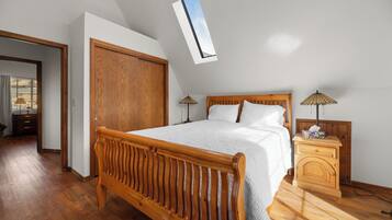 Une chambre à coucher avec un lit en bois, une table de chevet, une lampe et une vue sur le ciel grâce à une lucarne.