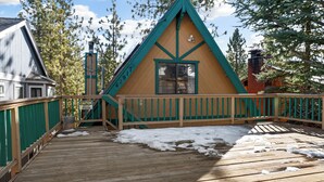 A wooden cabin with a green roof and a balcony, surrounded by trees and snow on the ground. - Little Bear Lodge (Big Bear Lake)