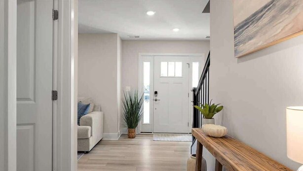 A hallway with a wooden floor, a white door, a beige sofa, and a wooden bench with a potted plant.