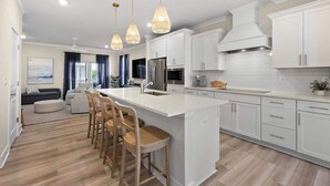 A modern kitchen with white cabinetry, a large island with bar stools, and pendant lighting.