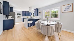 A modern kitchen with dark blue cabinets, a central island, and a round dining table with chairs. - Coastal Modern Retreat | Large Group Getaway on 2 Acres (Arnold)