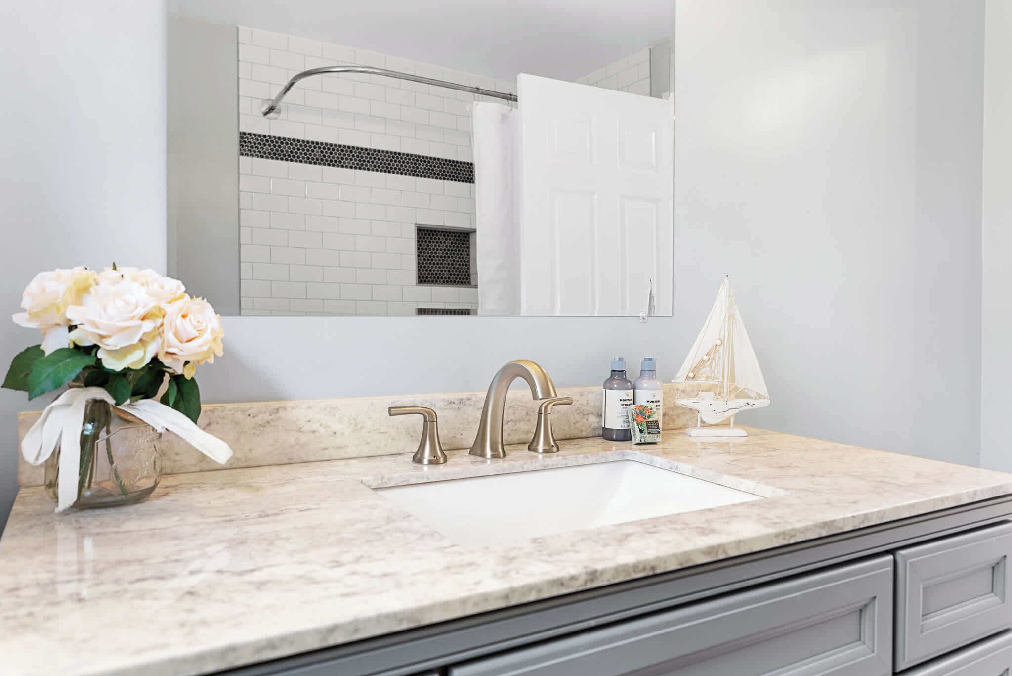 A bathroom with a white sink, a mirror, a shower curtain, and a vase with flowers.