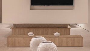 Ein modernes Wohnzimmer mit einem großen Flachbildfernseher an der Wand, einer Holzunterhaltungseinheit darunter und zwei weißen, skulpturalen Vasen auf dem Boden.