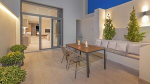 Eine Terrasse im Freien mit einem Holztisch und -stühlen, einem weißen Sofa und Blumentöpfen.