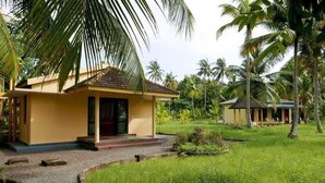 A yellow building with a tiled roof, surrounded by lush greenery and palm trees. - Lake Vechoor Villas By BRDGE HOSPITALITY (Kottayam)