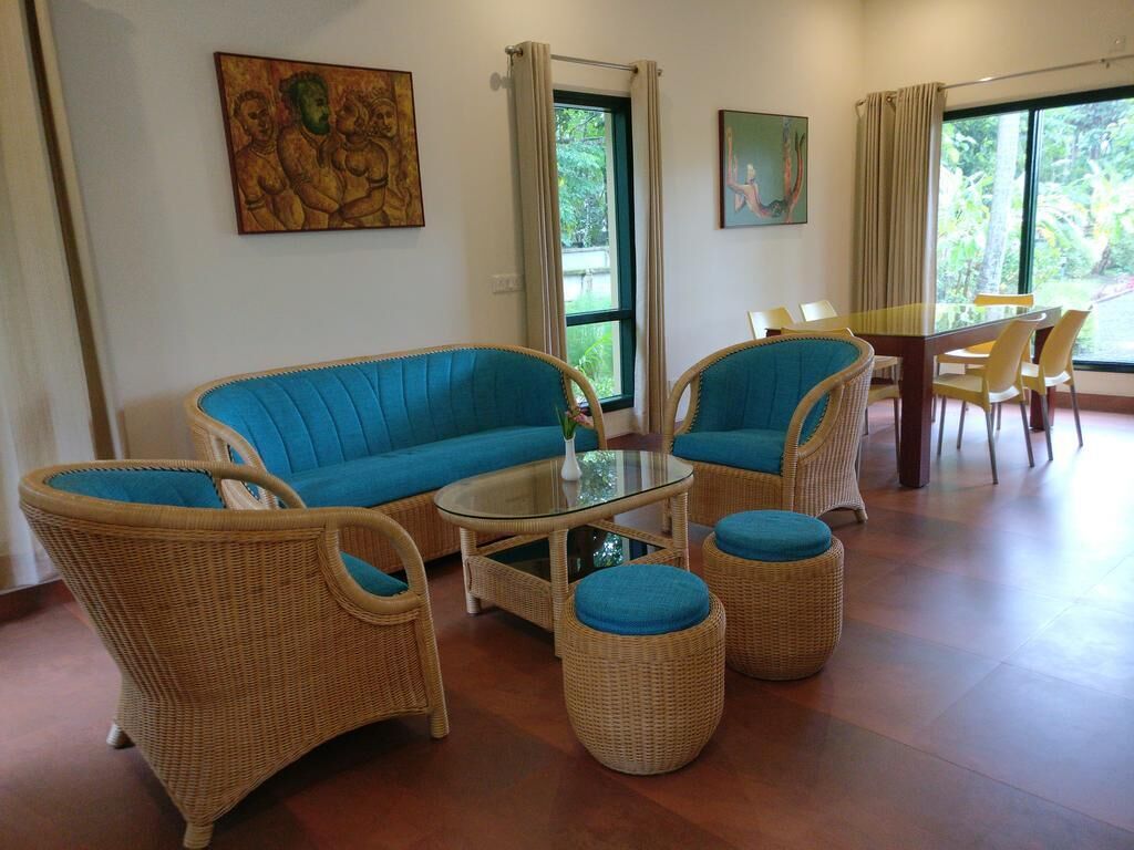 Una habitación con muebles de mimbre, una mesa de centro de vidrio y dos ventanas con cortinas.