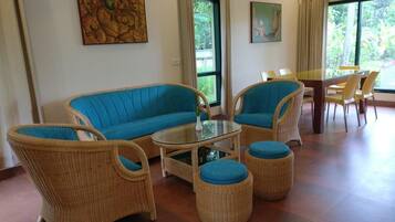 Una habitación con muebles de mimbre, una mesa de centro de vidrio y dos ventanas con cortinas.