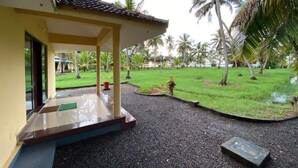 A covered outdoor area with a gravel path leading to a building entrance, surrounded by palm trees and a grassy lawn. - Lake Vechoor Villas By BRDGE HOSPITALITY (Kottayam)