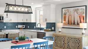 Una cocina moderna con armarios blancos, un salpicadero tipo espiga, una zona de comedor con sillas azules y un mueble decorativo con detalles tallados.