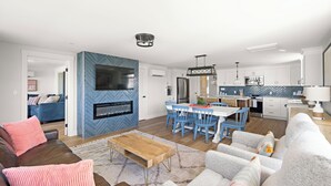 Una sala moderna con chimenea, un comedor con sillas azules y una cocina con armarios blancos.
