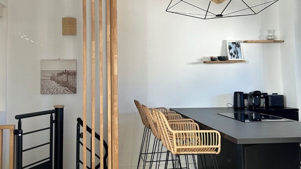 A modern kitchen with a central island, wooden chairs, a black countertop, and a hanging light fixture.