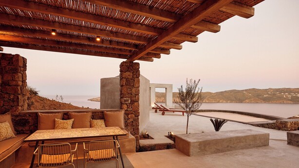 Un patio al aire libre con una mesa, sillas, un pilar de piedra y vista al mar.