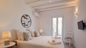Un dormitorio con una cama grande, dos mesitas de noche, un televisor montado en la pared y una ventana con cortinas.