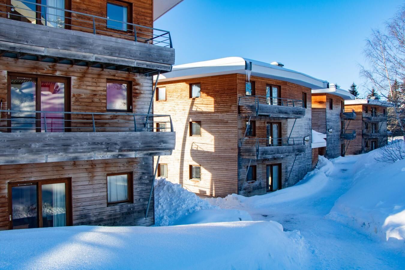 A multi-story wooden building with balconies and large windows, surrounded by snow.