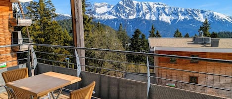 A balcony with a table and chairs, a view of snow-capped mountains, and a building with a sign.