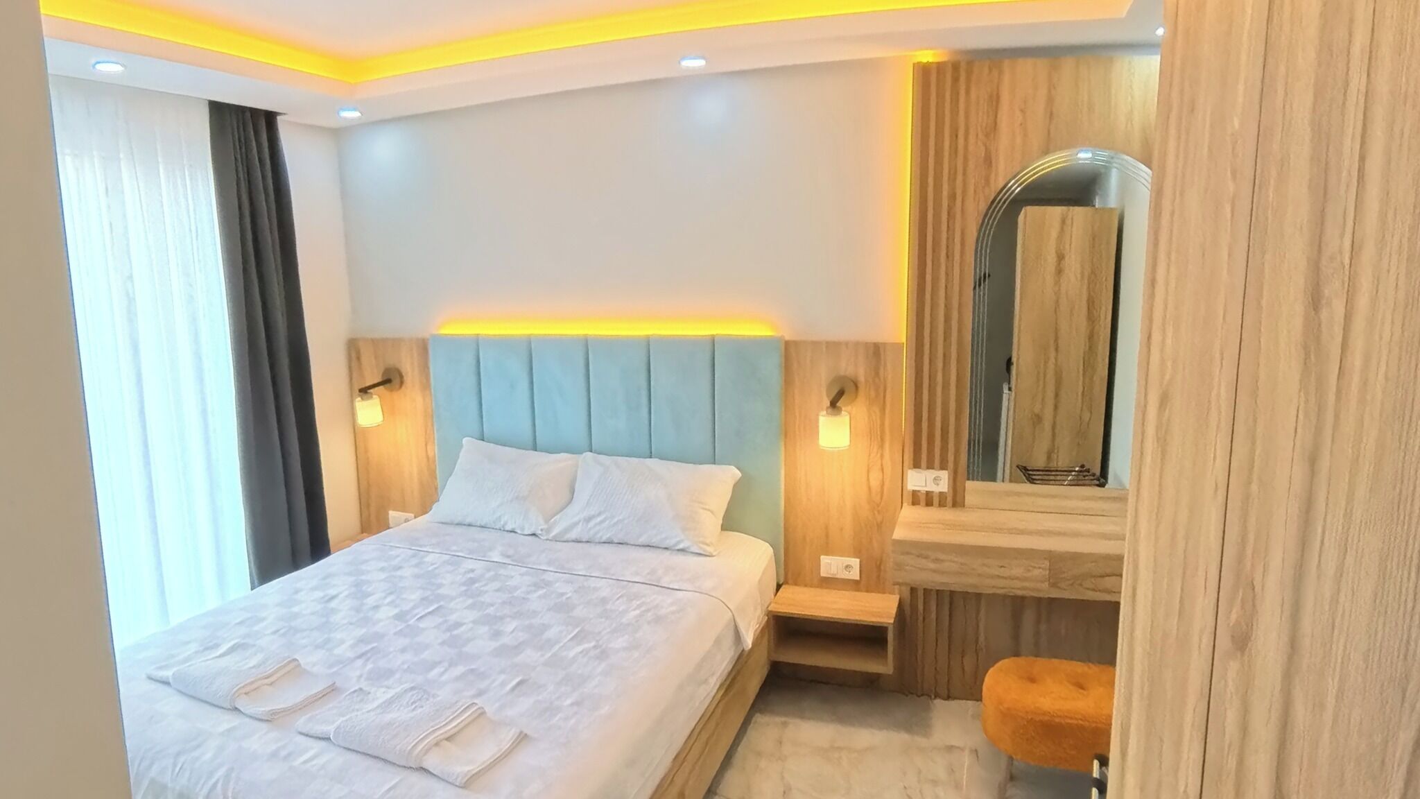 A modern hotel room with a large bed, bedside tables, a mirror, and a bench.