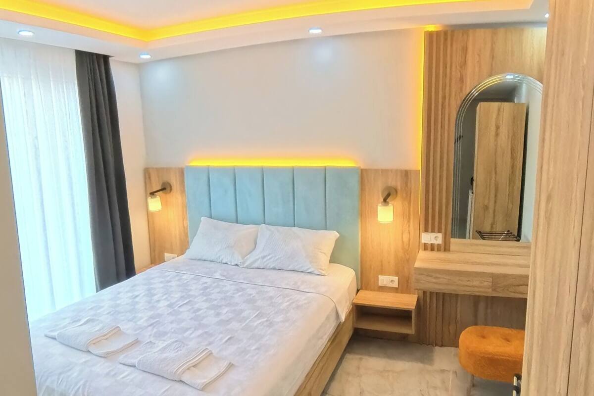 A modern hotel room with a large bed, bedside tables, a mirror, and a bench.