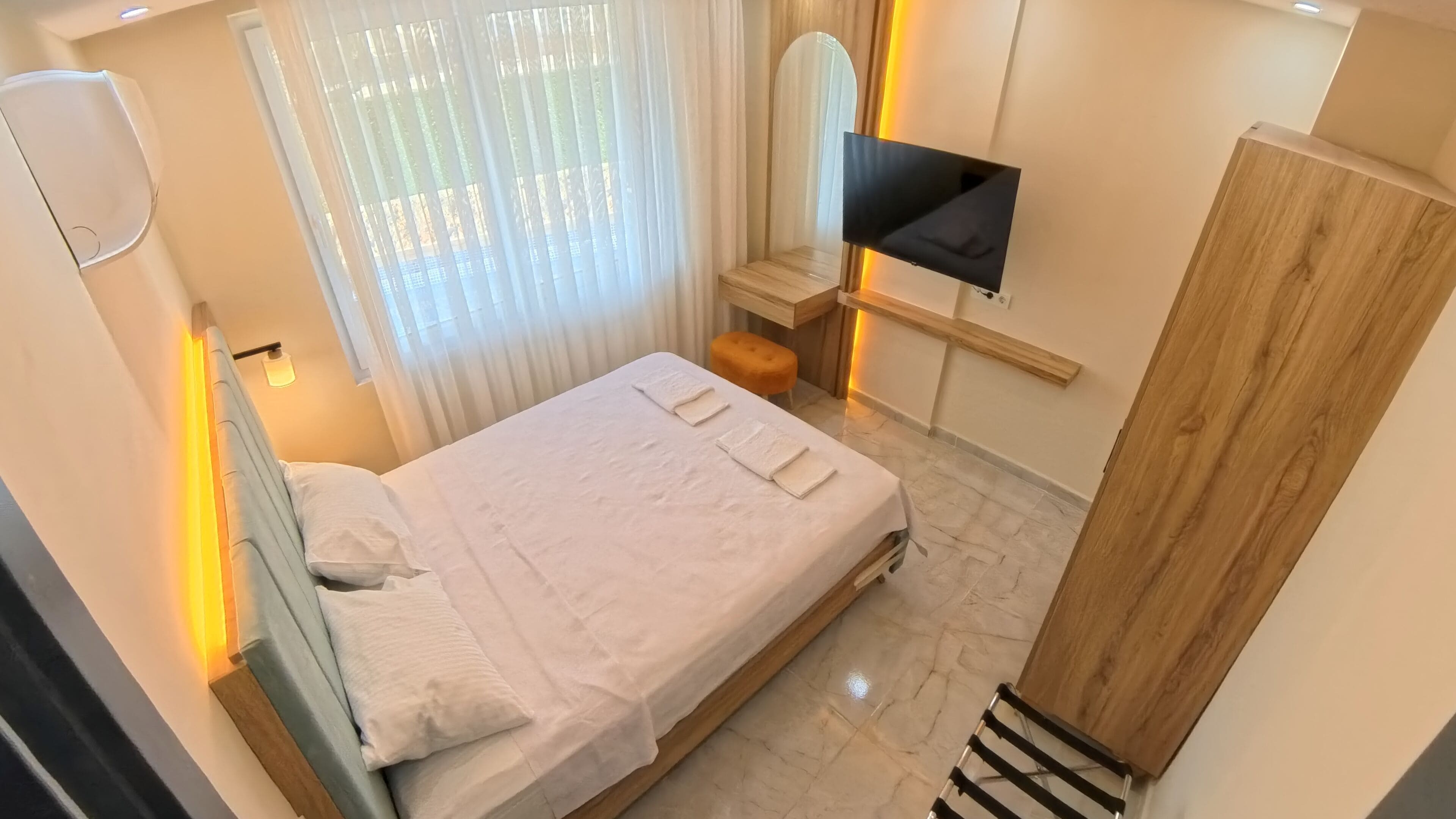 A neatly arranged bedroom with a bed, a TV mounted on the wall, and a wooden wardrobe.