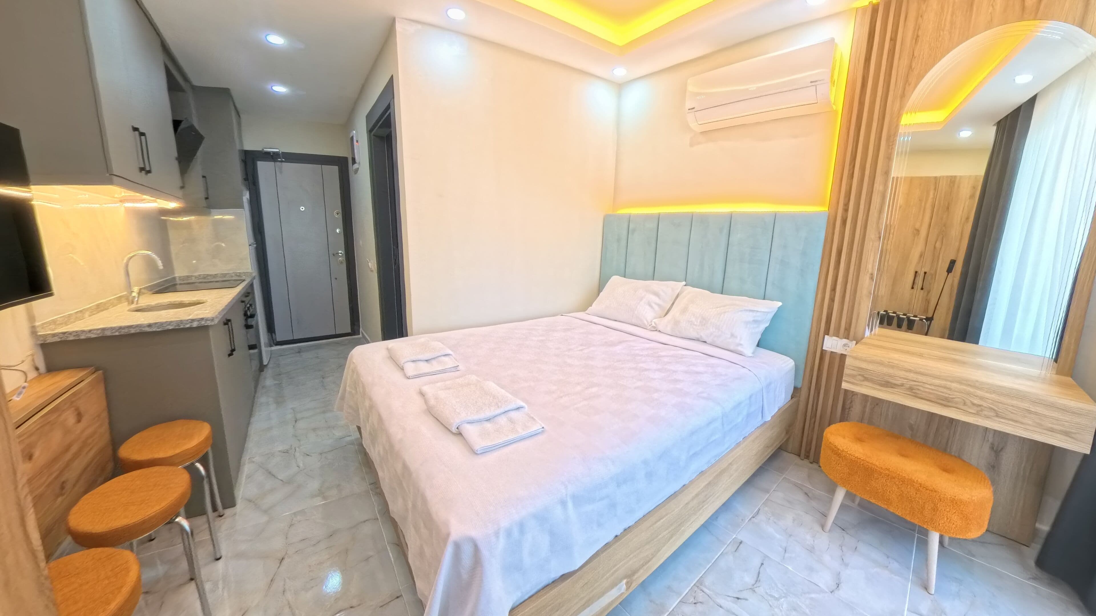 A modern hotel room with a bed, a desk, a mirror, and a bathroom.